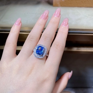 Macro shot of cushion-cut blue gemstone ring with double halo diamond setting on finger