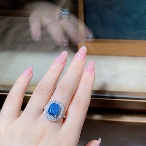 Detailed view of a silver ring featuring a cushion-cut blue gem and double halo of diamonds