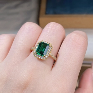 Macro detail of emerald cut green gemstone ring with halo diamonds on golden band