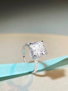 Close-up of Asscher cut moissanite ring with pave diamonds on blue silk ribbon