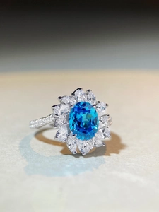 Detail of flower-shaped silver ring with oval blue gemstone and surrounding halo of zircons