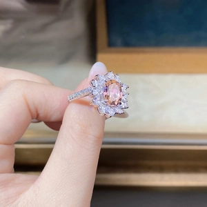 Detailed close-up of a flower-shaped ring featuring a pink orange gemstone and zircon accents