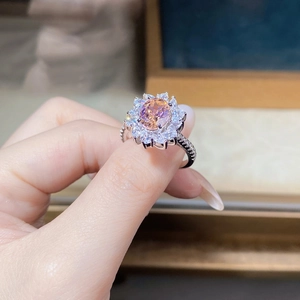 Close-up of a flower-shaped ring with a pink-orange oval gemstone on a woman's finger