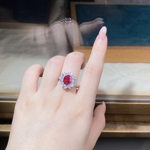 Close-up of pigeon blood red oval ruby ring with floral diamond cluster setting on finger
