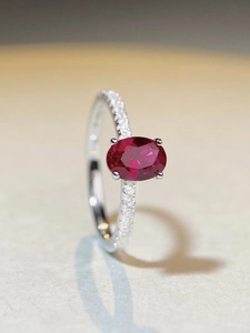 Macro shot of oval red ruby S925 silver ring with small side diamonds and four-prong setting