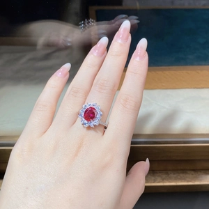 Detail shot of an oval ruby red gemstone ring worn on finger with floral halo setting