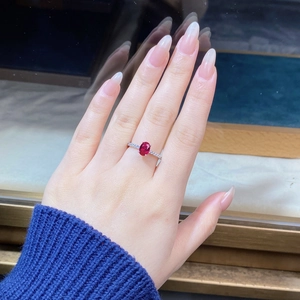 Macro shot of an oval ruby ring with side diamonds on a silver band worn on hand