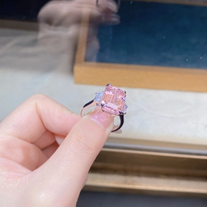Macro shot of an emerald-cut pink zircon ring with side stones held by a person