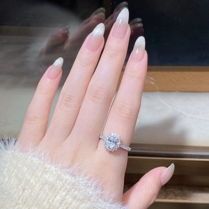 Close-up of a halo engagement ring with an oval moissanite stone worn on a finger