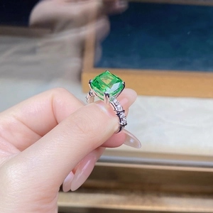Macro shot of emerald cut green stone set in split shank silver band with micro pave