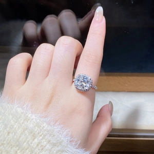 Macro shot of 5 carat cushion cut moissanite halo ring on finger with pavé band detail