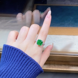 Detail of square cut emerald ring with side stones worn on finger with blue sweater