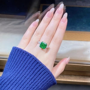 Close-up of a cushion-cut emerald ring with sparkling side stones on a silver band