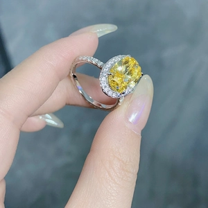 Detailed view of an oval yellow gemstone ring with pavé diamond halo on a finger