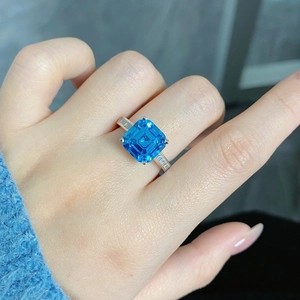Macro shot of silver ring featuring a large square blue gemstone on a finger