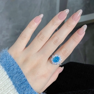 Macro detail of oval blue high carbon diamond ring with sunflower halo on model finger