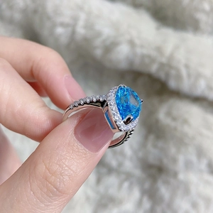 Macro shot of silver ring with pear-cut blue gemstone and halo diamond settings