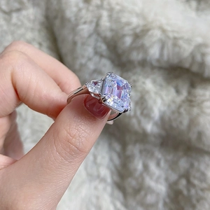 Emerald cut high carbon diamond ring on hand over soft white faux fur background