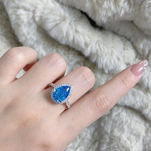 Close-up of a pear-shaped blue sapphire ring with halo diamond setting on a plush background