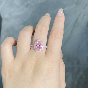 Gros plan d'une bague halo rose ovale avec diamants sur la main, finition argentée
