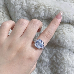 Detailed close-up of emerald cut stone ring with pear shaped side accents on soft fur