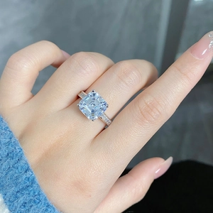 Close-up of Asscher cut light blue gemstone ring with baguette side stones on a finger