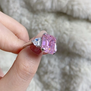 Detail shot of an emerald-cut pink gemstone ring with triangle side stones on hand
