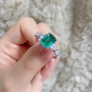 Macro view of emerald-cut green gemstone ring with sparkling side diamonds on plush fabric
