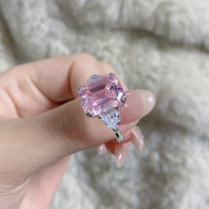 Macro shot of an emerald-cut pink gemstone ring with triangle side diamonds on soft fabric