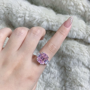 Close-up of emerald-cut pink gemstone ring with teardrop side stones worn on finger