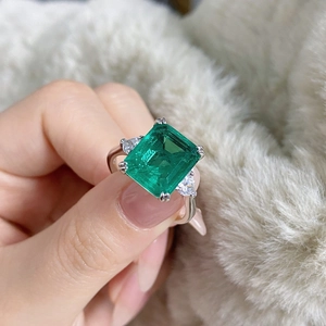 Detailed view of an emerald cut green gemstone ring with pear side stones on hand