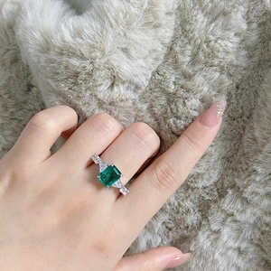 Detailed view of an emerald-cut green gemstone ring with side stones on a silver band