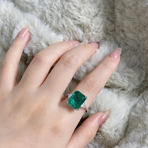Macro shot of an emerald-cut green stone ring with side diamonds on a soft textured surface