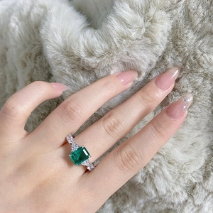 Close-up of an emerald-cut green stone ring with side diamonds on a female finger