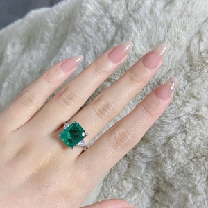 Close-up of S925 silver ring with emerald-cut green stone on a soft white fur backdrop