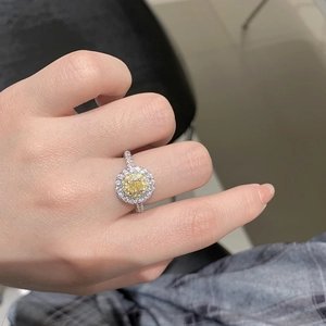 Close-up of yellow oval halo ring with sparkling zircon and silver band on finger
