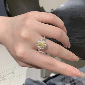 Macro detail of oval yellow zircon ring with silver halo setting worn on finger