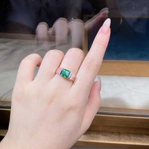Detail of emerald cut green gemstone ring with blue side stones on silver band