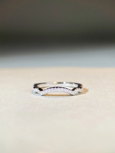 Close-up of a silver wave V-shaped ring with pavé-set zircons on a beige background