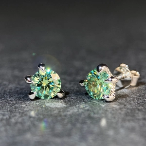 Dettaglio macro di orecchini a lobo in moissanite verde tonda con tre griffe argento