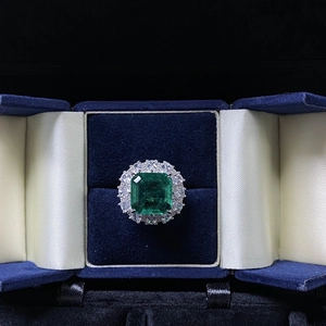 Macro shot of an emerald-cut green gemstone ring with a halo of white zircon diamonds