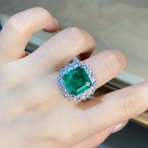 Macro close-up of emerald-cut green stone ring with dual-layer halo diamond setting