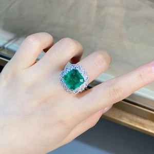 Detailed view of an emerald-cut green stone ring with double halo pavé setting on finger