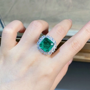 On-hand display of luxurious emerald cut green gemstone ring with white halo diamonds