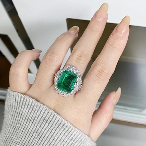 Close-up of a luxury emerald cut green gemstone ring with halo diamond setting on finger
