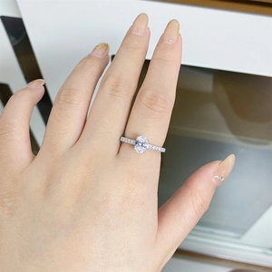 Close-up of an oval-cut moissanite ring with a pavé diamond band on a finger