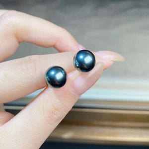Close-up of polished black Tahitian pearl earrings held by hand showing smooth texture