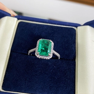 Macro view of emerald-cut green gemstone ring with halo diamonds in a navy velvet box