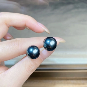 Elegant pair of round black Tahitian pearls with high luster held between fingers