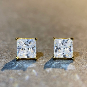 Macro shot of princess cut moissanite stud earrings in a classic gold four-prong setting